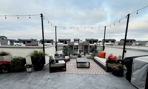 A rooftop terrace with a sofa set, a coffee table, potted plants, and string lights. - Ocean View Luxury Condo off Monterey Bay Brand New (Marina)