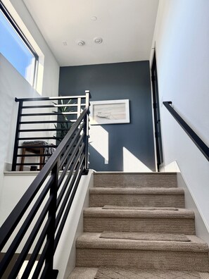 A staircase with a black railing, carpeted steps, and a framed picture on the wall. - Ocean View Luxury Condo off Monterey Bay Brand New (Marina)