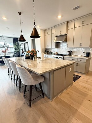 A modern kitchen with a central island, bar stools, pendant lighting, and stainless steel appliances. - Ocean View Luxury Condo off Monterey Bay Brand New (Marina)
