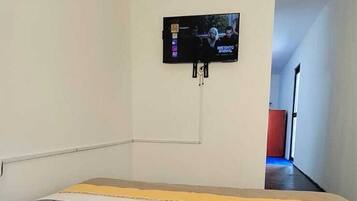 Una habitación con una cama, un televisor montado en la pared y un control remoto sobre la cama.