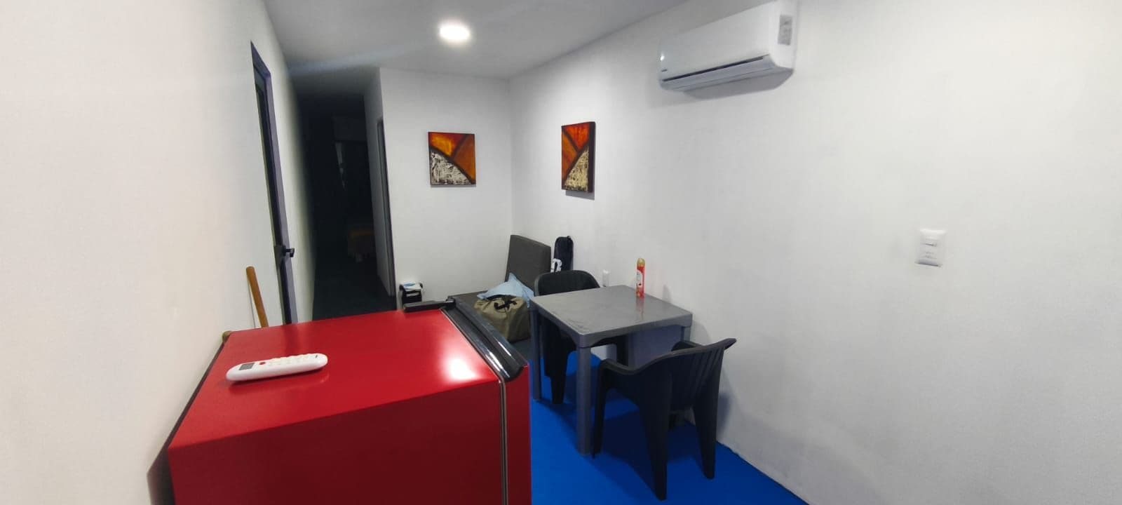 A small room with a red cabinet, a grey table, a black chair, and a white air conditioner on the wall.