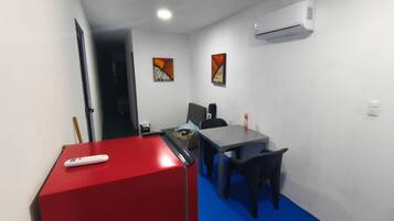 A small room with a red cabinet, a grey table, a black chair, and a white air conditioner on the wall.