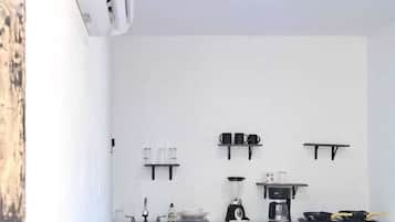 Una kitchenette compacta con encimera blanca, cafetera, licuadora y un lavamanos pequeño.