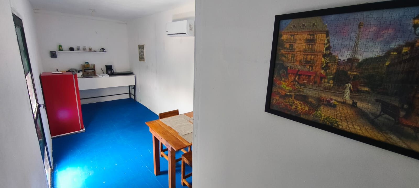 A room with a blue floor, a wooden table, a red cabinet, and a wall-mounted air conditioner.