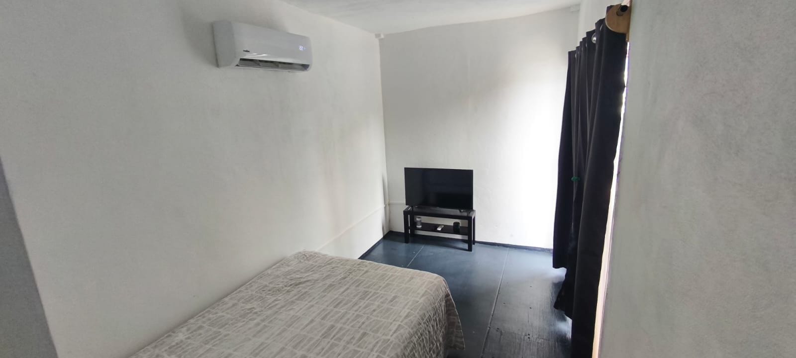A room with a bed, a television on a stand, and an air conditioning unit on the wall.