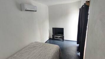 A room with a bed, a television on a stand, and an air conditioning unit on the wall.