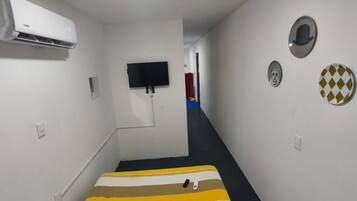 A narrow hallway with a bed, a mounted television, and wall decorations.