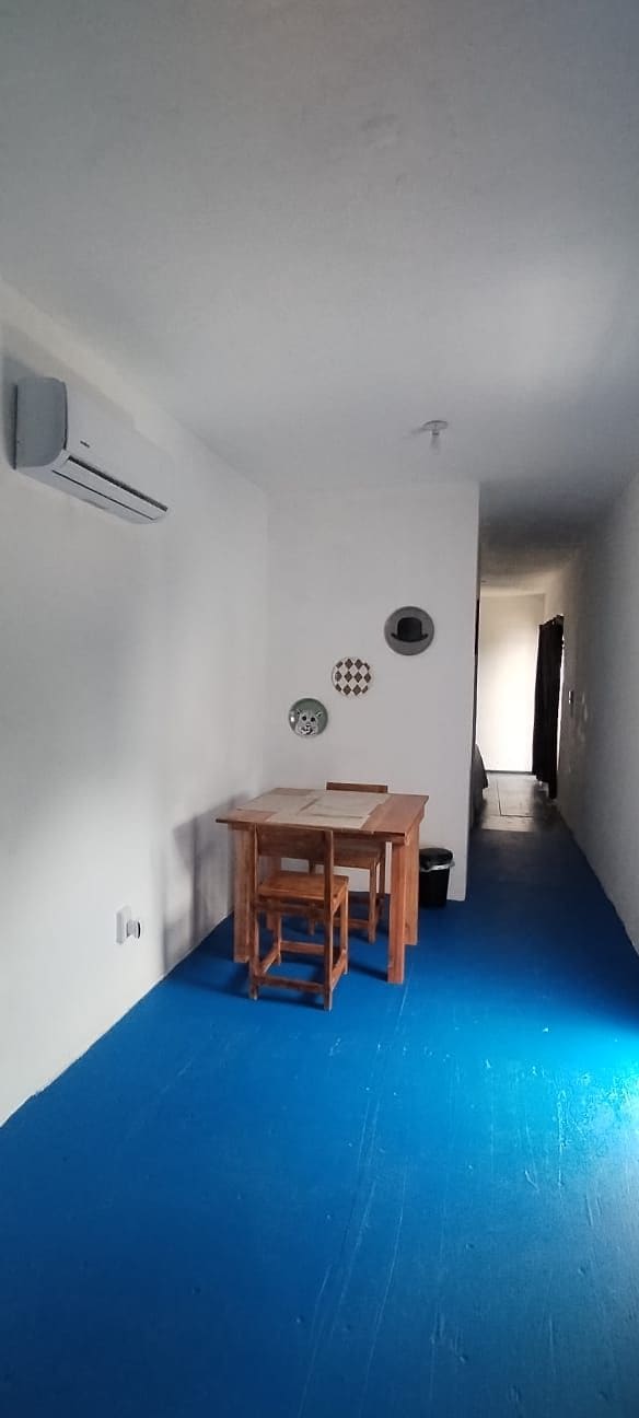 Una habitación con piso azul, una mesa de madera con sillas, un aire acondicionado instalado en la pared y una puerta que da a otra habitación.