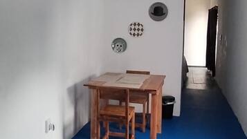 Una habitación con piso azul, una mesa de madera con sillas, un aire acondicionado instalado en la pared y una puerta que da a otra habitación.