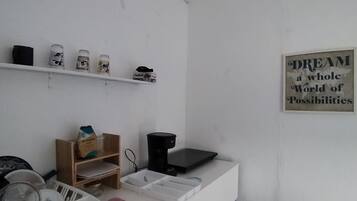 Una habitación con pared blanca, estante con varios objetos, cafetera y un cartel motivacional.