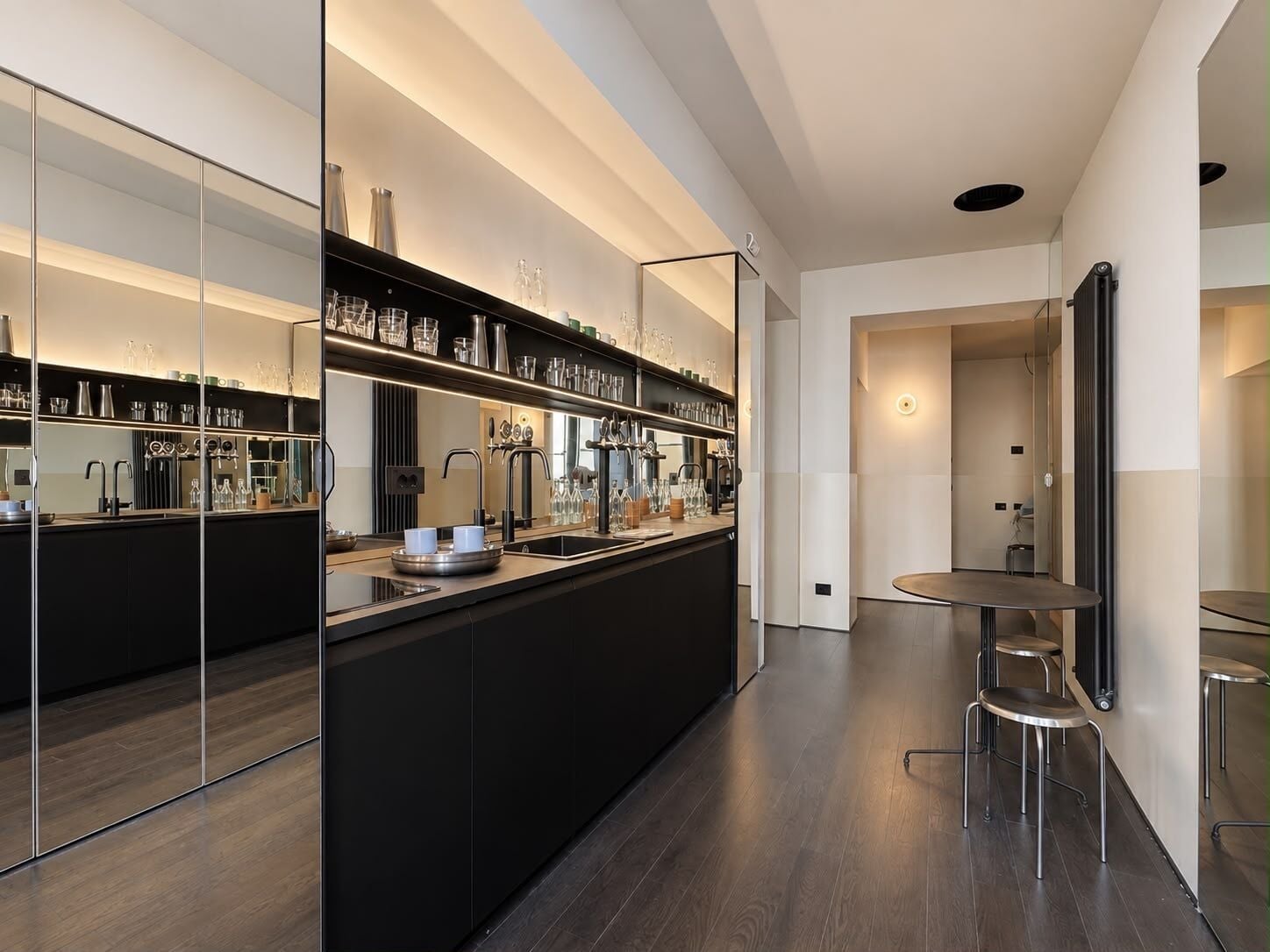 A modern kitchen with a central island, mirrored backsplash, and a dining area with a round table and stools.