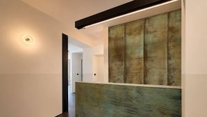 A modern hallway with a wooden floor, a wall-mounted light fixture, and a large textured wall panel.