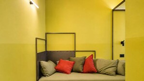 A room with a sofa against a yellow wall, a metal frame structure, and a small light fixture.