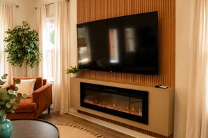A living room with a flat-screen TV mounted above a fireplace, a sofa, and a potted plant. - Talk of TownHome! (Indian Springs Village)