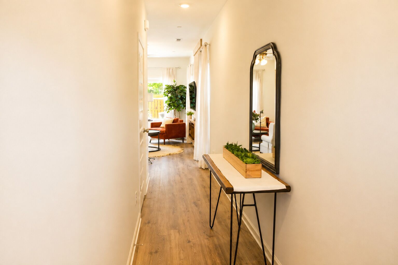 A hallway with a wooden floor, a console table with a mirror, and a plant.