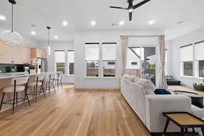 Eine moderne Küche mit Barhocker, ein Essbereich mit einer Couch und großen Fenstern.
