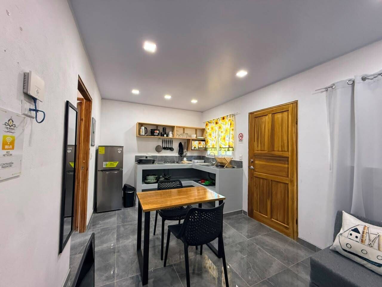 Una cocina compacta con comedor, refrigerador, pileta y puerta de madera.