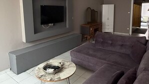 A living room with a large flat-screen TV mounted on the wall, a grey sofa, a small round coffee table, and a ceiling fan. - No 19 By Suite Daire (Istanbul)