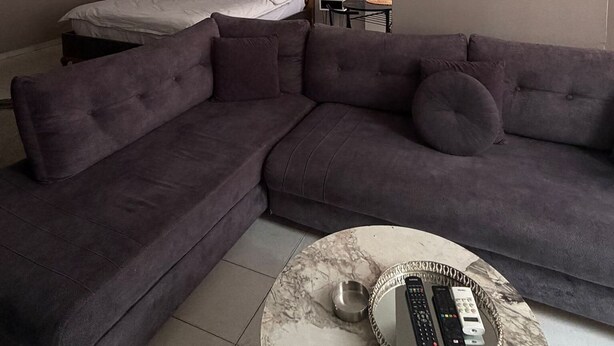 A modern living room with a sectional sofa, a bed with a wooden headboard, a round coffee table with a remote control, and a pendant light. - No 19 By Suite Daire (Istanbul)