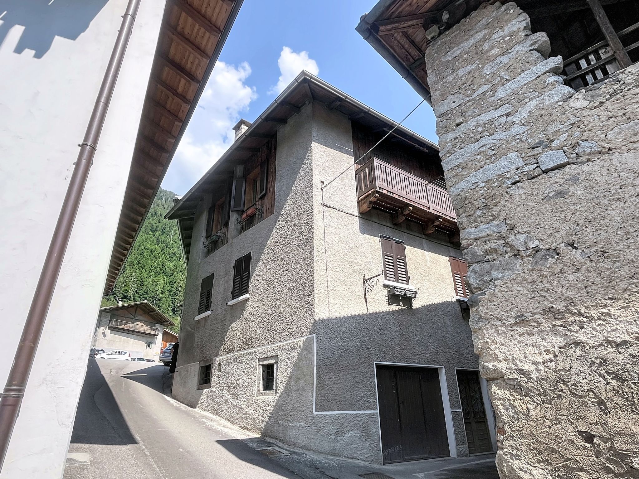 A narrow street with a stone building featuring a wooden balcony and a small window.