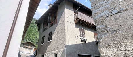 A narrow street with a stone building featuring a wooden balcony and a small window.