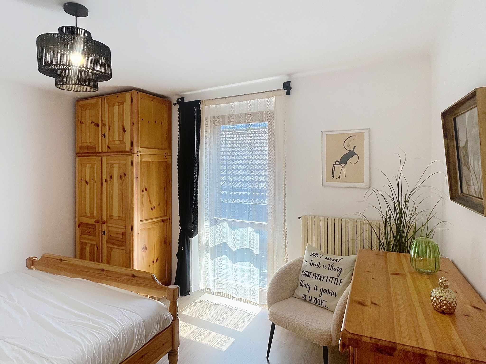 A bedroom with a wooden wardrobe, a bed, a table with a vase, and a chair.