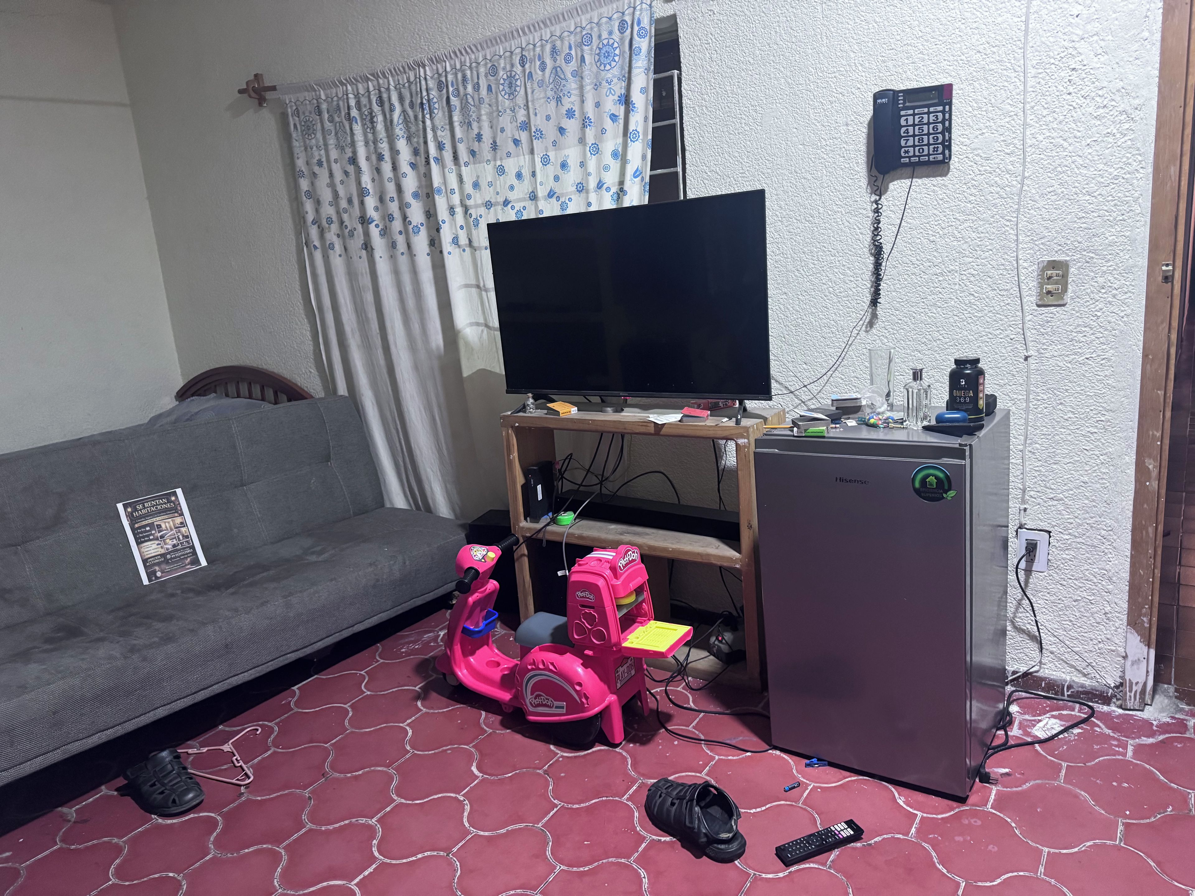 A living area with a sofa, a television, a small refrigerator, and a child's scooter.