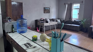 A living room with a sofa, a coffee table, a water dispenser, a large water bottle, a plant, and a fruit bowl. - HOSTALa (Tala)