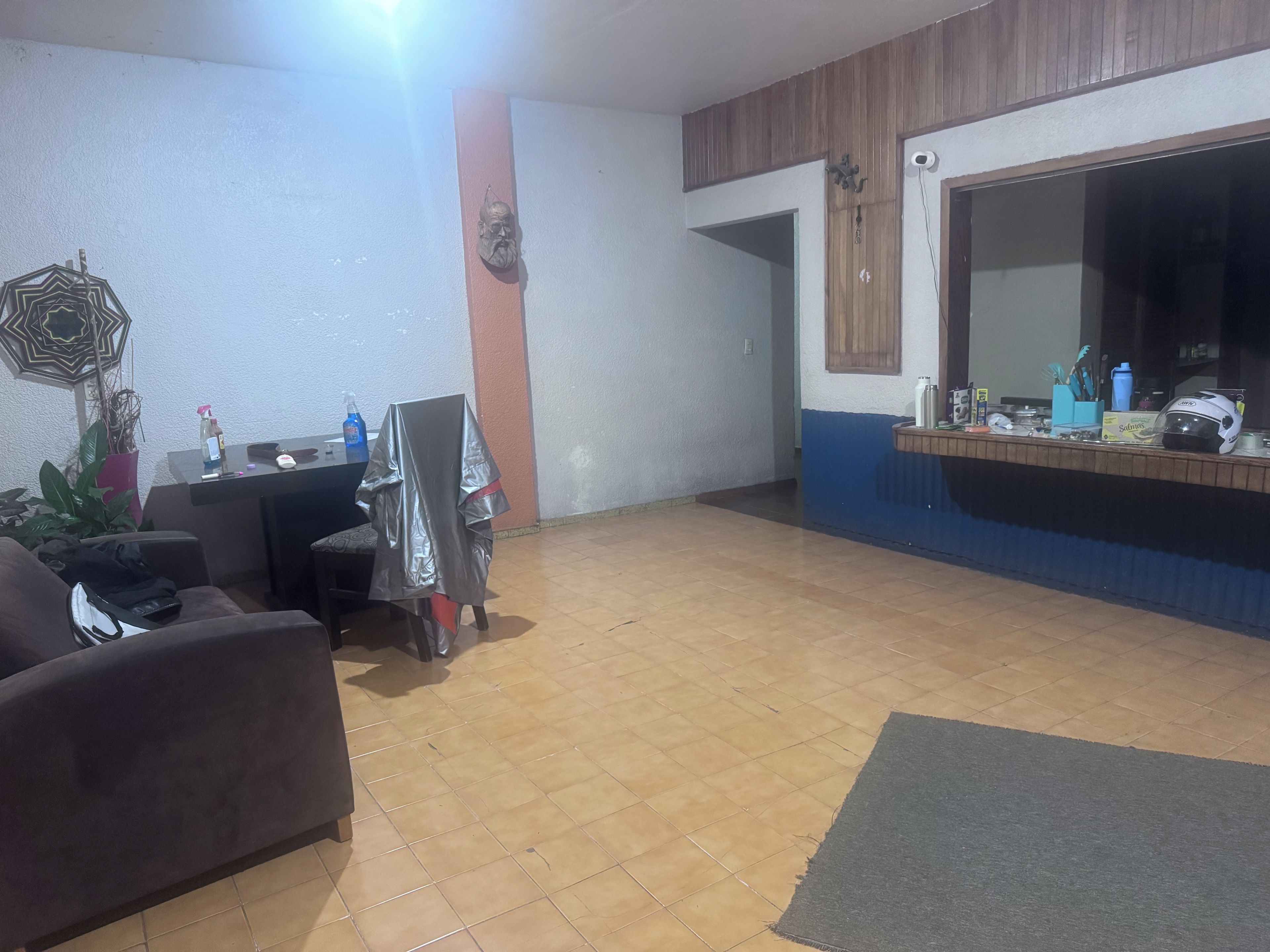Una sala de estar con un sof á, una mesa de centro y un televisor. Se observa un mueble de madera y piso con baldosas.