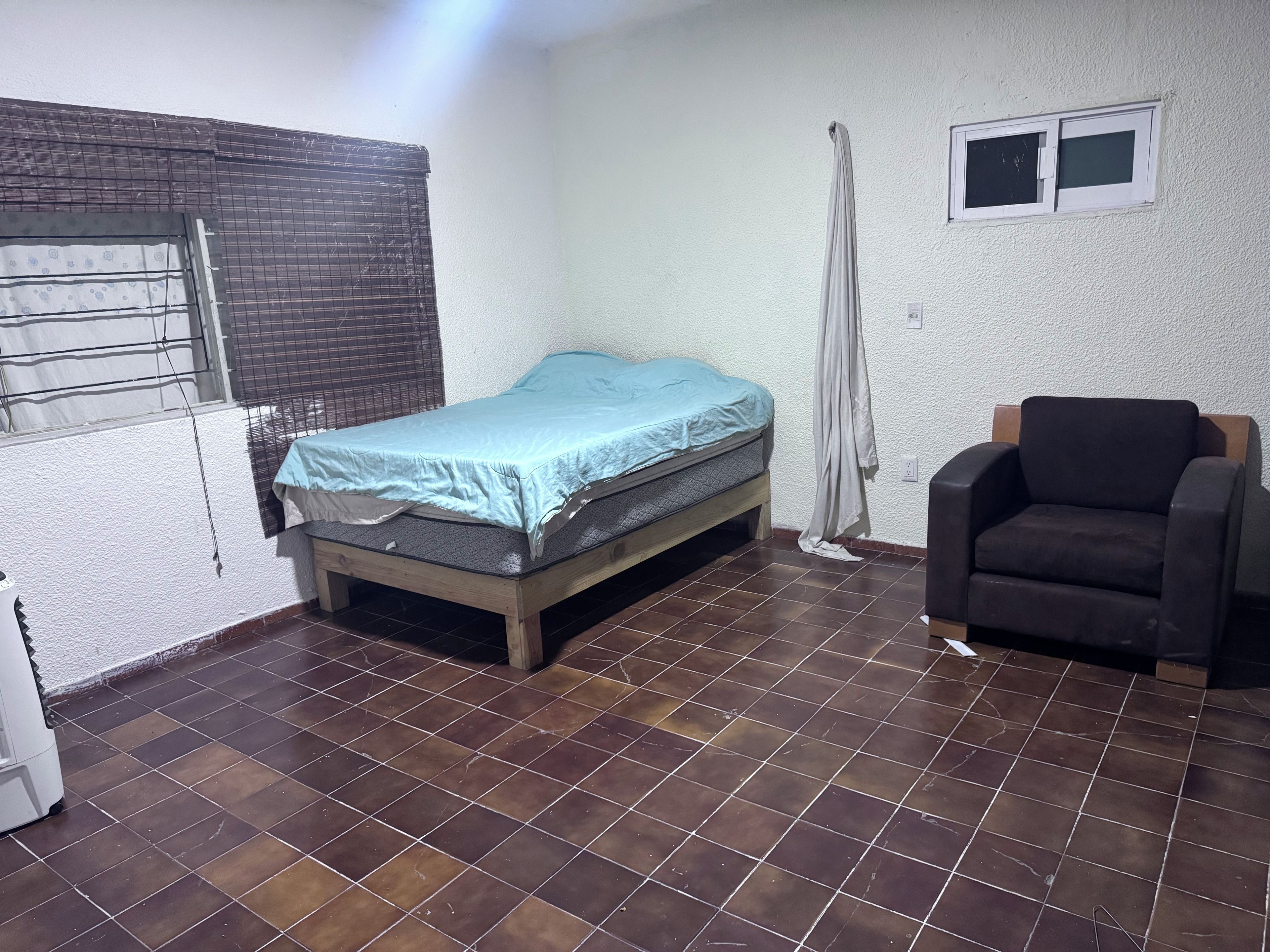 A room with a bed, a chair, a radiator, and a window with a curtain.