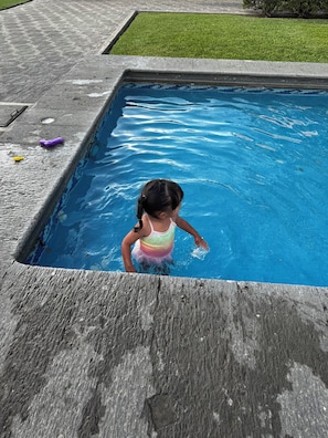 A child in a swimming pool with a wooden deck and grass in the background.