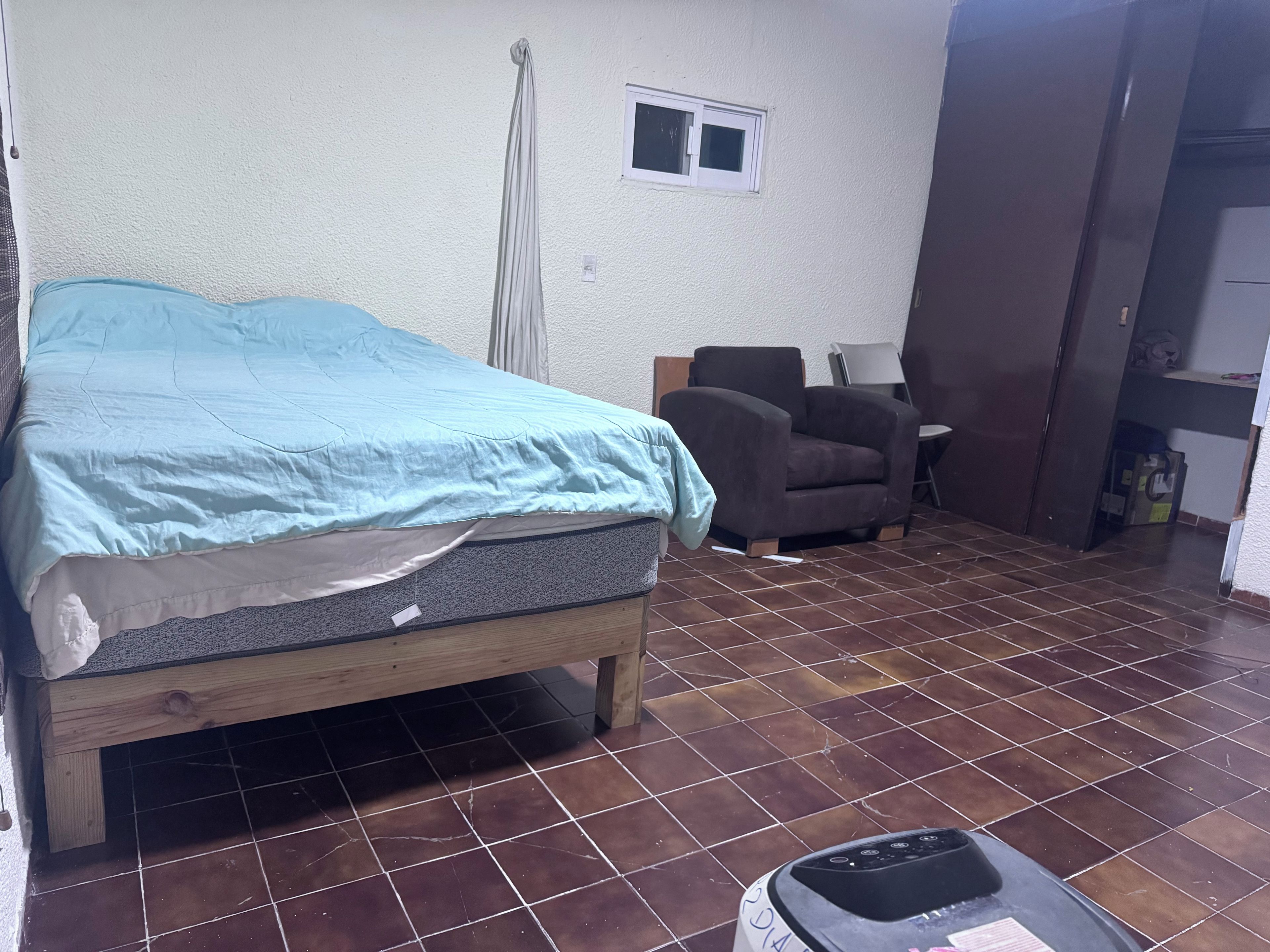 Een kamer met een bed, een stoel, een klein tafeltje en een kast.