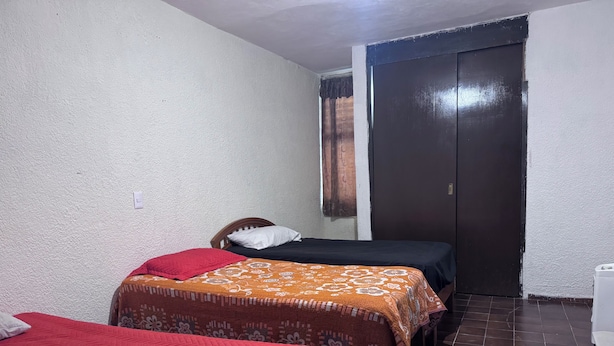 A small, single-room accommodation with two beds, a wardrobe, and a tiled floor. - HOSTALa (Tala)