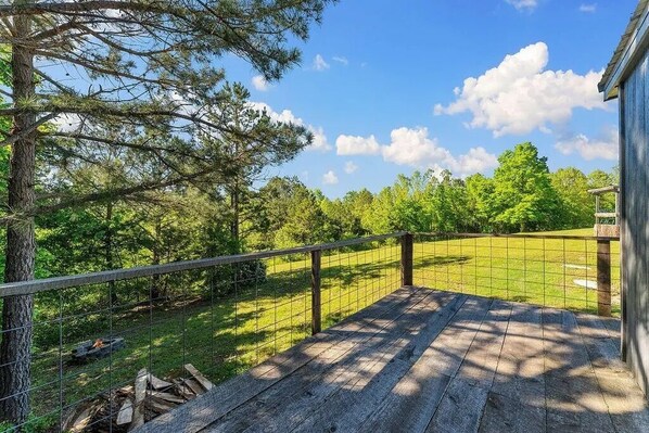 A wooden deck with a metal railing overlooking a grassy area with trees. - The Adventure Center (Pineville)