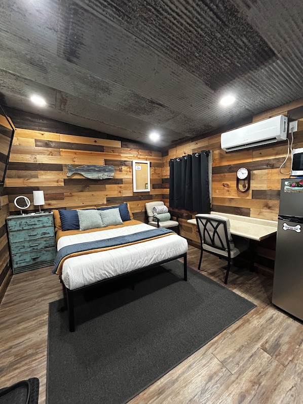 Een slaapkamer met een bed, nachtkastje, stoel, bureau en een koelkast.