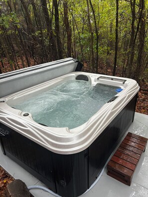 Een hottub in een bebost gebied met een houten bank ernaast.
