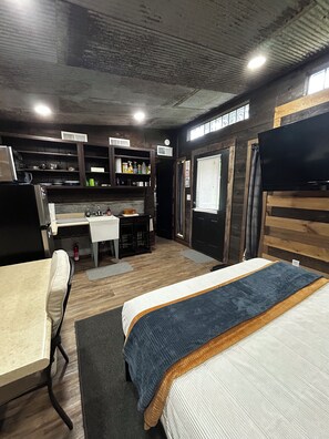 Een kleine slaapkamer met een bed, een bureau en een kitchenette.
