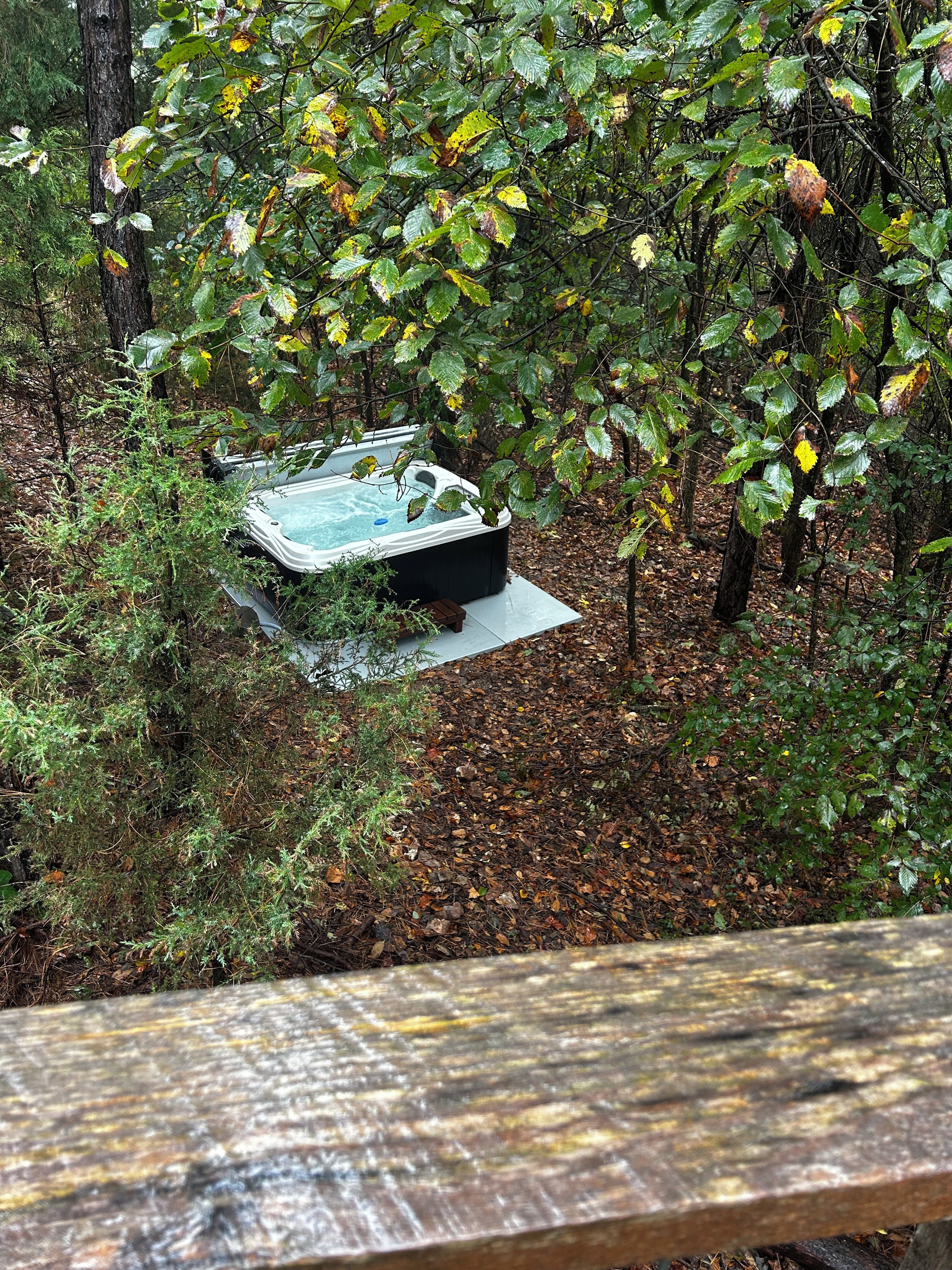 A hot tub in a wooded area with a wooden deck in the foreground.