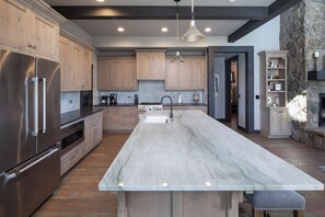 A spacious kitchen with a large marble island, stainless steel appliances, and wooden cabinets.