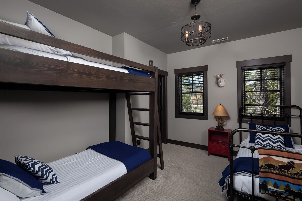A bunk bed room with a ladder, a red nightstand, and a window with a view of trees.