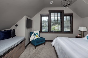 Une chambre avec un lit superposé, un lit simple, une chaise, un téléviseur et une fenêtre avec des stores.