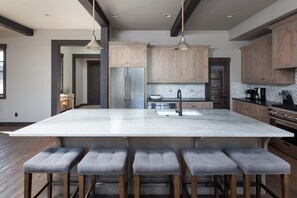 Une cuisine moderne dotée d’un grand îlot central, de tabourets de bar, d’armoires en bois et d’appareils électroménagers en acier inoxydable.
