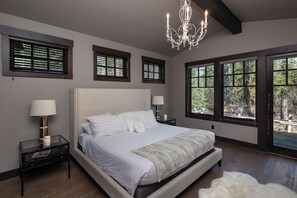 Une chambre à coucher avec un grand lit, deux tables de chevet, un lustre et de nombreuses fenêtres donnant sur l’extérieur.