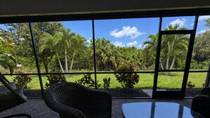 Une pièce dotée d'une grande fenêtre, de meubles en osier et offrant une vue sur un jardin tropical.