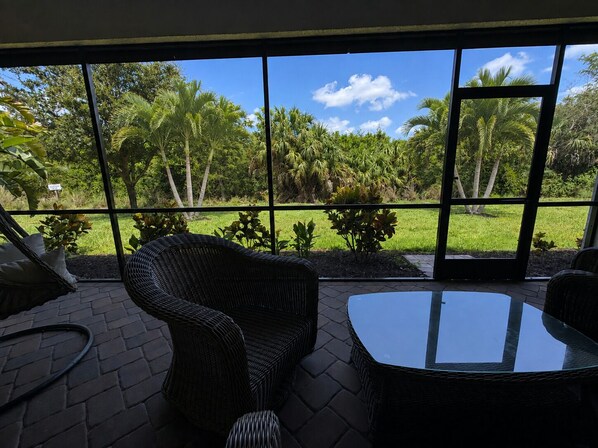 A room with a large window, wicker furniture, and a view of a tropical garden. - Naples Retreat with FREE Level 2 EV Charging + Resort Amenities (Naples)