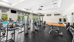 Une salle de sport équipée de divers appareils d’exercice, dotée d’un ventilateur au plafond et de grandes fenêtres donnant sur une piscine.