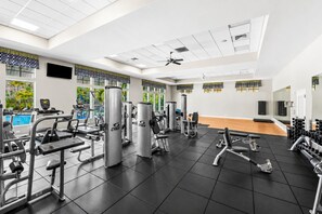 Une salle de sport équipée de divers appareils d’exercice, dotée d’un ventilateur au plafond et de grandes fenêtres donnant sur une piscine.