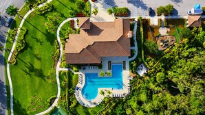 Une grande maison avec une piscine, entourée de pelouses et d’arbres bien entretenus.