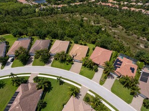 An aerial view of a residential area with houses, a curved road, and surrounding greenery. - Naples Retreat with FREE Level 2 EV Charging + Resort Amenities (Naples)