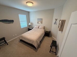 Ein Schlafzimmer mit einem Bett, Nachttischen, einem Fenster mit Jalousien, einem Wandbild und einer Tür.